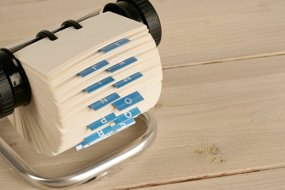 A close-up of a traditional Rolodex with alphabet tabs on a wooden desk
